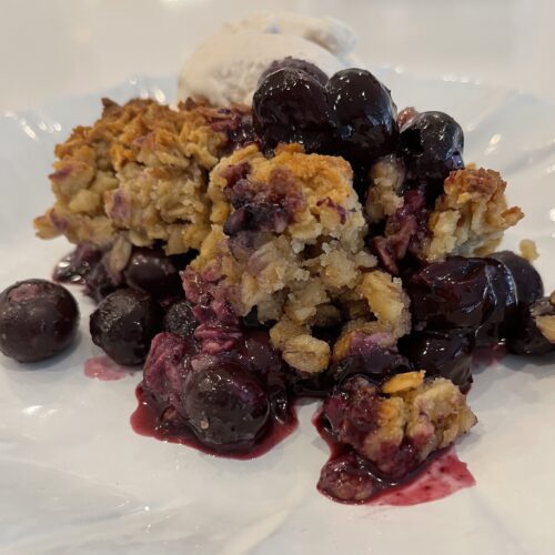 Side view photo of Healthy Blueberry Cobbler served on a white plate with vanilla ice cream.