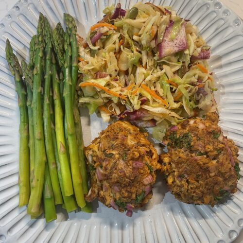 2 Vegan Mushroom Crab Cakes on a plate with a salad and asparagus.