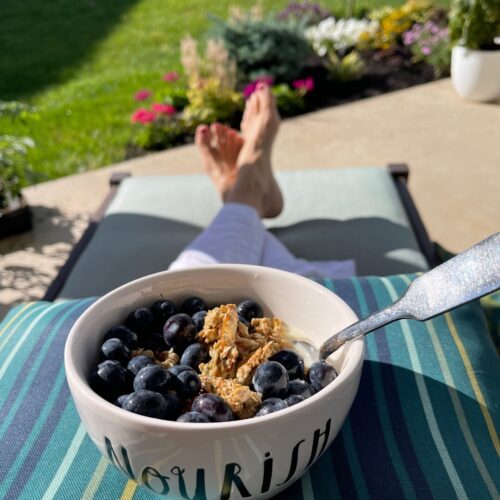 A person sitting outdoors on a lounge chair eating Quick and Easy Homemade Granola with Blueberries.